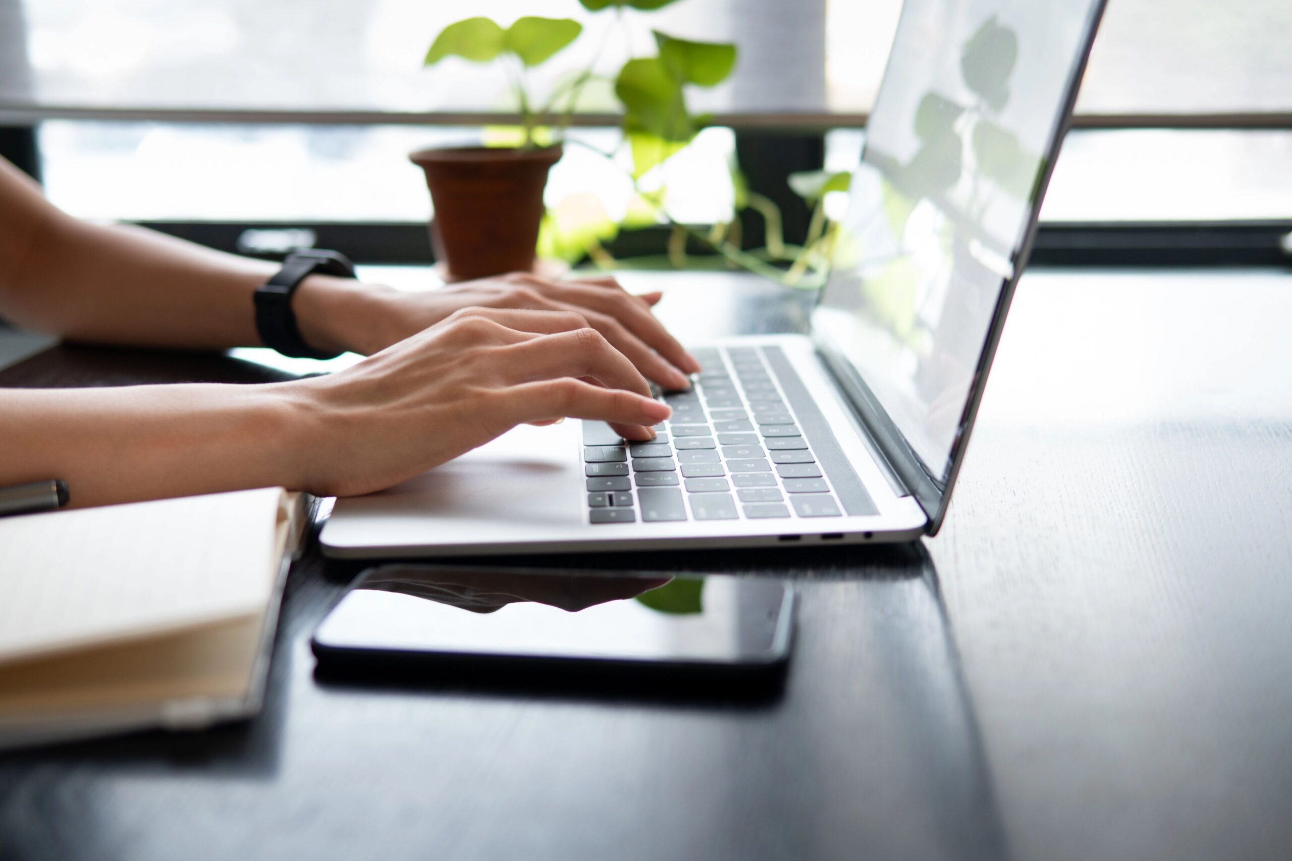 Person typing on laptop with plant and smartphone on desk, illustrating content strategy and digital marketing.