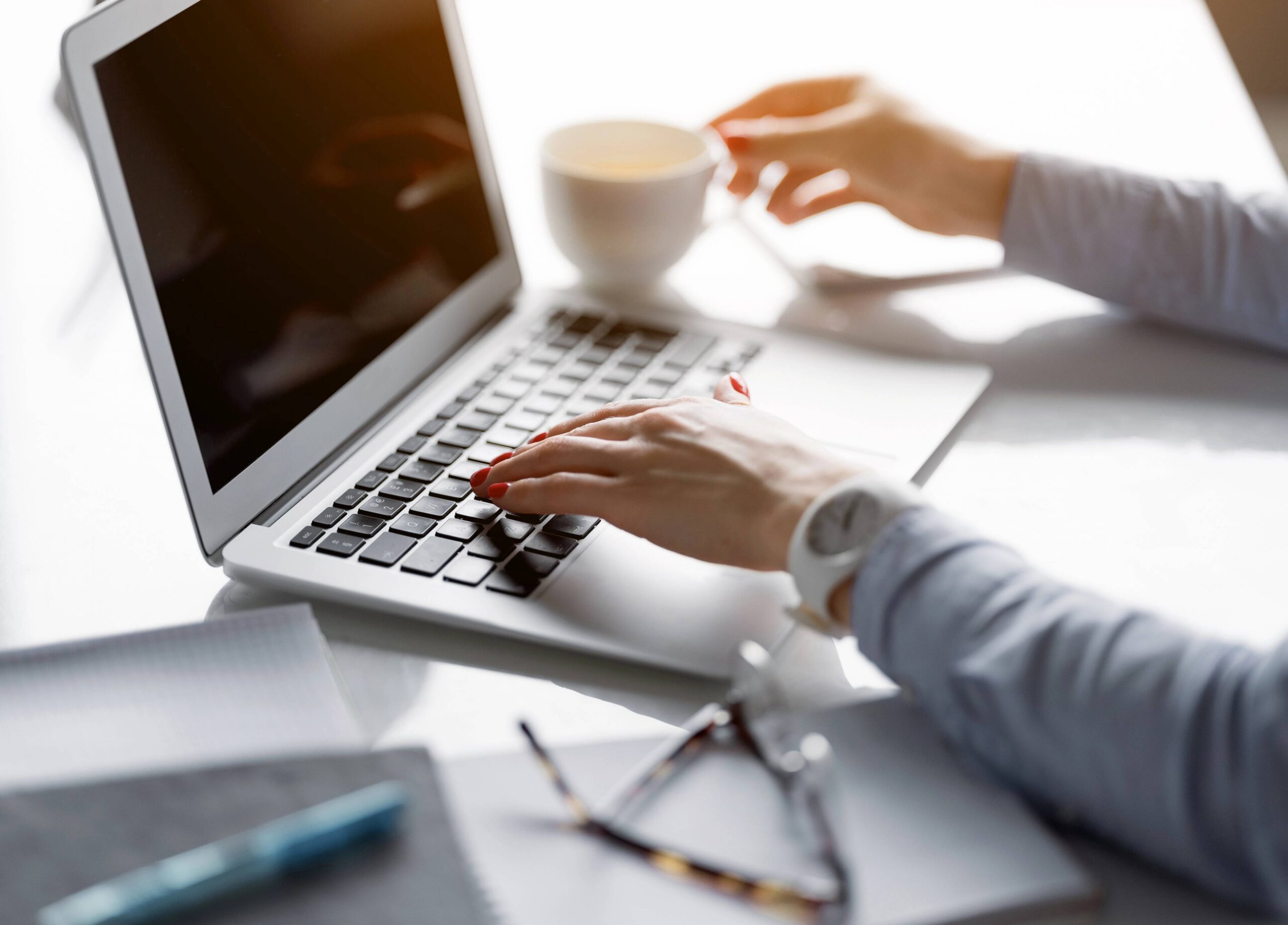 Person typing on laptop with coffee cup, surrounded by notebooks and glasses, illustrating content creation and marketing strategy.