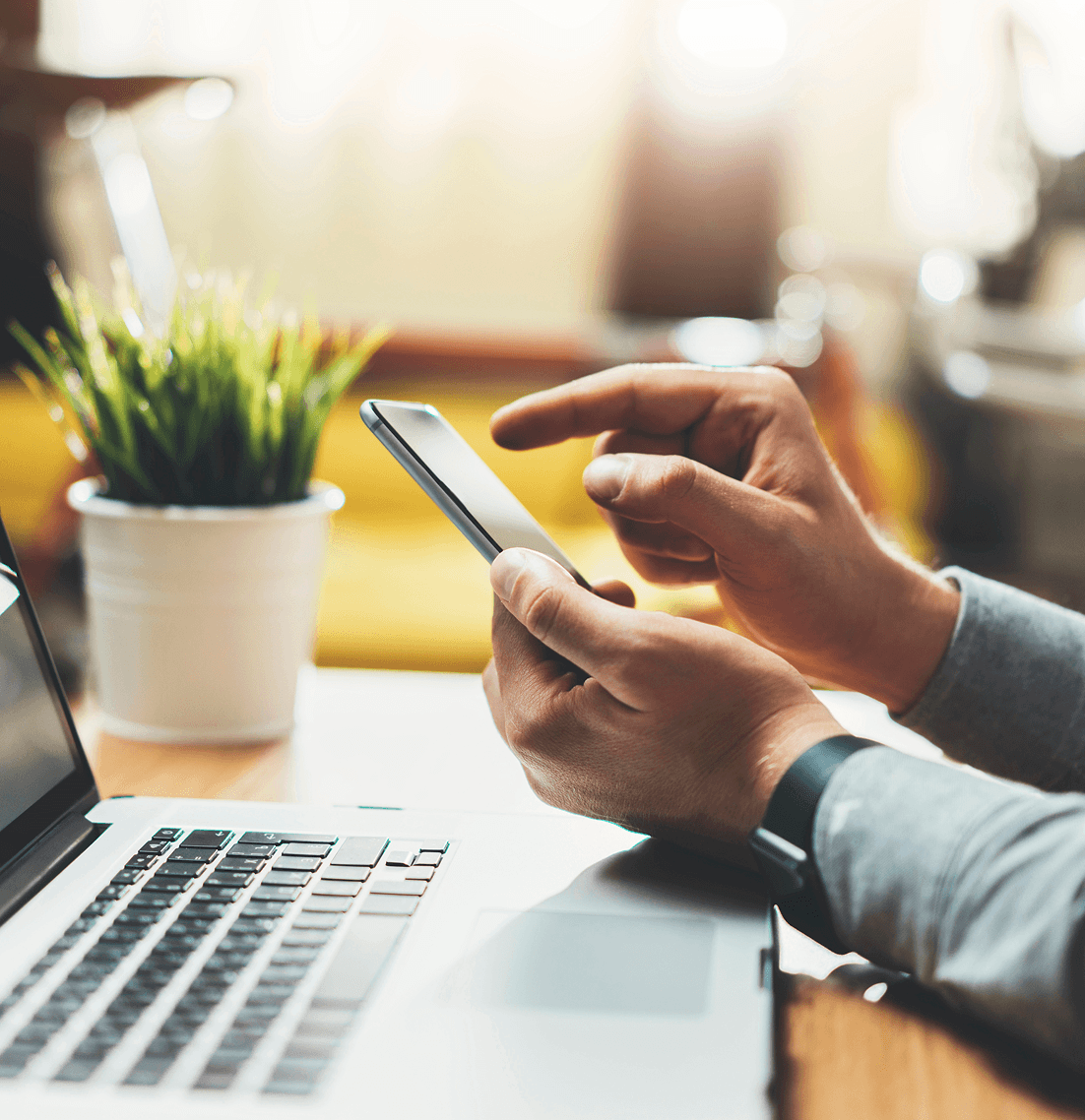 Hands holding a smartphone while interacting with a laptop, symbolizing digital marketing engagement and strategy adaptation for small businesses.